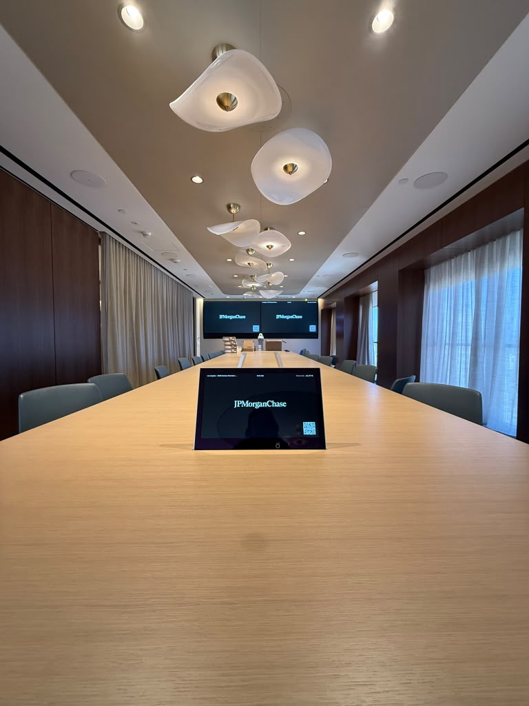 Executive boardroom with a long table, sculptural pendants and dual displays for video conferencing