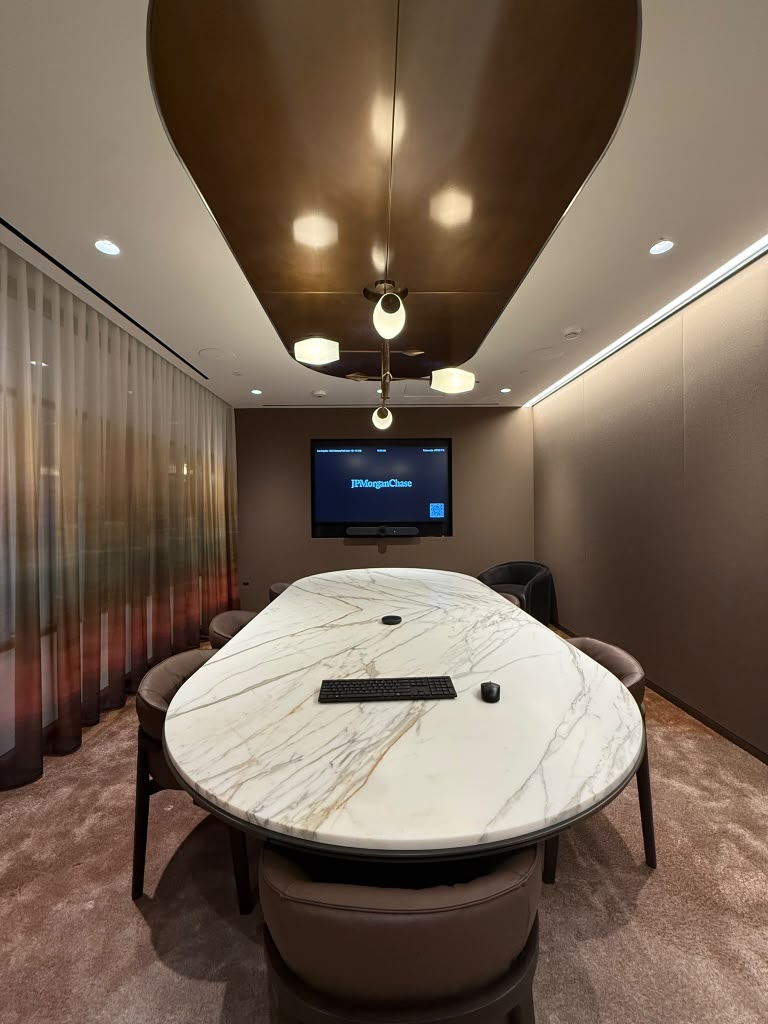 Private meeting room with a marble oval table, bronze ceiling feature and a wall display