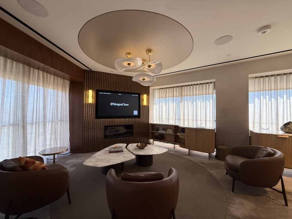 Private client lounge with a wall display above a linear fireplace, a sculptural glass chandelier, marble tables and leather armchairs